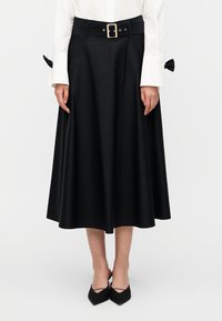 Μαύρη φούστα μέχρι το γόνατο με φαρδιά ζώνη μέσης, θηλιές για ζώνη και χρυσή αγκράφα. Ομαλή υφή με δύο πλαϊνές τσέπες και λεπτομέρεια φιόγκου στο πίσω μέρος.