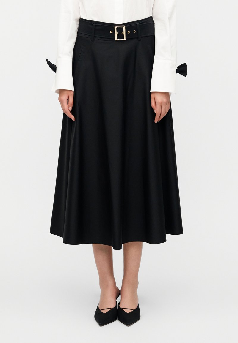 Μαύρη φούστα μέχρι το γόνατο με φαρδιά ζώνη μέσης, θηλιές για ζώνη και χρυσή αγκράφα. Ομαλή υφή με δύο πλαϊνές τσέπες και λεπτομέρεια φιόγκου στο πίσω μέρος.