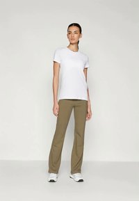 Witte t-shirt met korte mouwen gecombineerd met olijfgroene broek. Het model staat in sportschoenen en toont een eenvoudige, casual outfit.