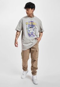 Grå oversized t-shirt med et farverigt astronautgrafik og tekst, parret med beige cargo bukser og hvide sneakers.