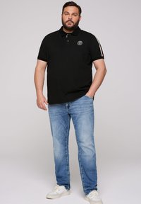 Czarny polo z małym logo, krótkim rękawem i białymi paskami, zestawiony z jasnoniebieskimi dżinsami i białymi trampkami.