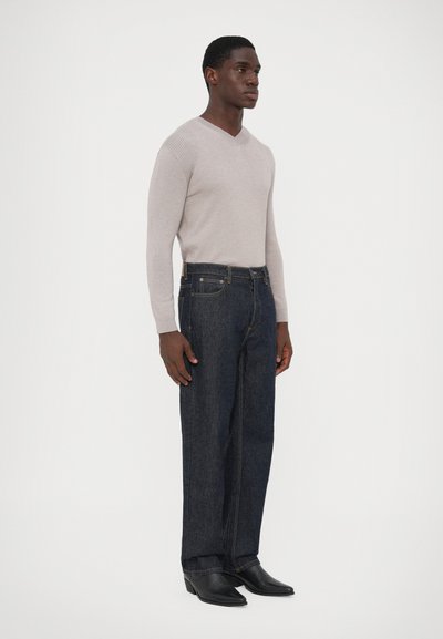 Svijetlosiva rebrasta v-izreza pulover, tamnoplave ravne traperice i crne čizme s oštrim vrhom. Ležerna odjeća s prilagođenim i strukturiranim siluetom.