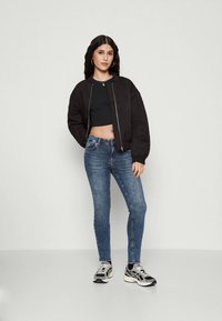 Chaqueta bomber negra, top negro corto, vaqueros azules ajustados y zapatillas negras/blancas. Telas suaves con colores distintivos y diseño casual.