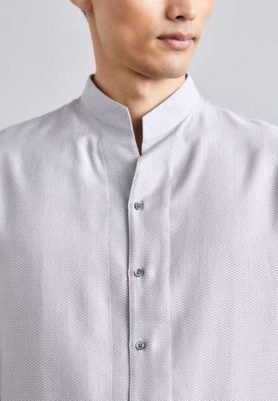 Camisa gris con un patrón y cuello mao, que presenta un sutil diseño de espiga, y tres botones en la parte delantera. Tejido ligero.