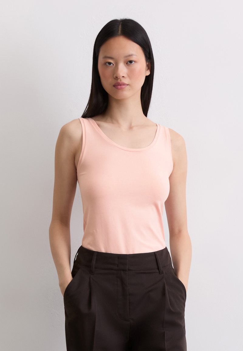 Lichtroze, mouwloze tanktop met een ronde hals, gemaakt van zachte stof; gecombineerd met hoge zwarte broeken.