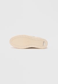 Sneaker sole in cream rubber with a textured, ridged pattern. Features a branded label on the side and a smooth, rounded shape.
