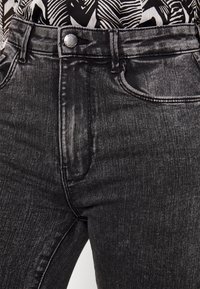 Close-up van zwarte high-waist jeans met een metalen knop en voorzakken, gecombineerd met een zwart-wit gestreept top.