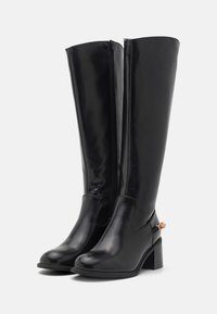 Botas negras hasta la rodilla hechas de material sintético brillante. Presentan un diseño elegante, tacón cuadrado, cremallera lateral y acentos decorativos en tono dorado.