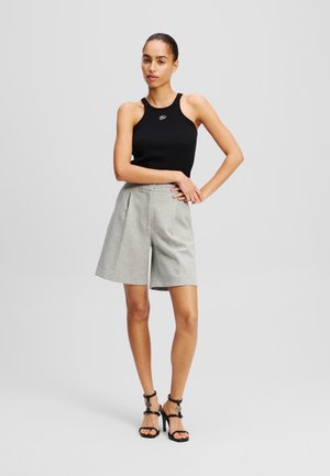 Black ribbed tank top with a small logo, paired with light gray tailored shorts featuring a waistband and pleats. Black strappy high heels.
