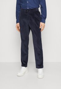 Navy corduroy trousers with a straight fit, featuring a button closure and textured vertical stripes, paired with white sneakers.