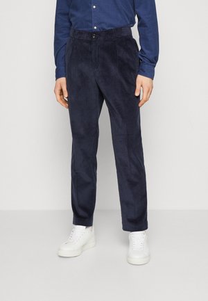 Marinblå kordbyxor med rak passform, som har en knappstängning och texturerade vertikala ränder, i kombination med vita sneakers.
