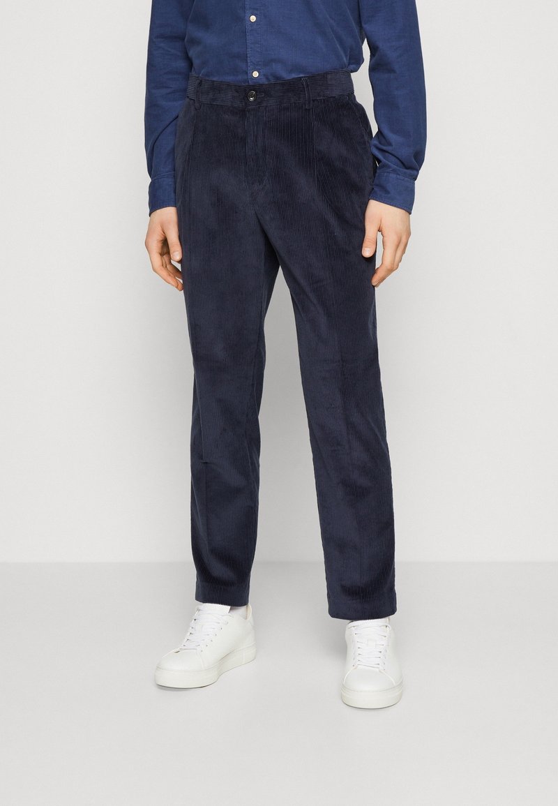 Navy corduroy trousers with a straight fit, featuring a button closure and textured vertical stripes, paired with white sneakers.