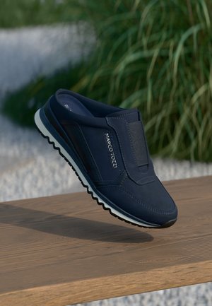 Zapato slip-on navy con parte superior texturizada, banda elástica y suela de goma blanca con un patrón en zigzag. Logo mostrado en el lado.