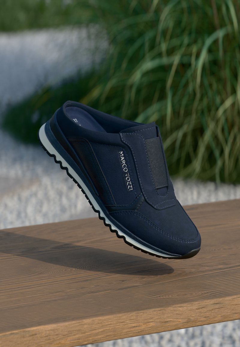 Ναυτικές παντόφλες με υφή στο άνω μέρος, ελαστική ταινία και λευκή καουτσούκ σόλα με ζιγκ-ζαγκ σχέδιο. Λογότυπο εμφανές στο πλάι.