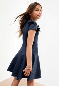 Rochie bleu marin cu mâneci scurte, accentuată cu detalii florale pe umeri, fustă evazată și textură netedă.