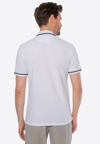 Bílá polo triko s krátkým rukávem, se černými akcentními pruhy na límci a manžetách rukávů. Měkký, hladký materiál, standardní střih.