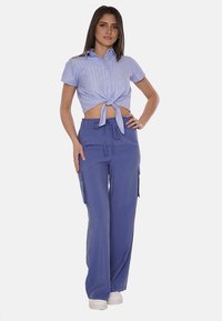 Camicetta corta a maniche corte a righe blu e bianche legata in vita, abbinata a pantaloni cargo blu a vestibilità ampia con tasche laterali.