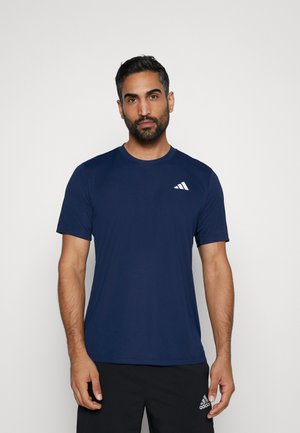 Camiseta deportiva de color azul marino, hecha de una tela suave, con cuello redondo, mangas cortas y un logo blanco en la parte superior izquierda del pecho.