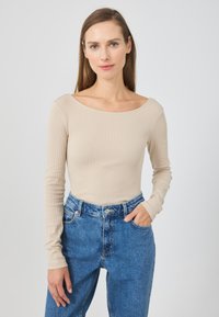 Dlouhý rukáv ribbed top v béžové barvě s širokým výstřihem, kombinovaný s modrými džíny vysokého pasu. Žádné viditelné vzory ani akcenty.