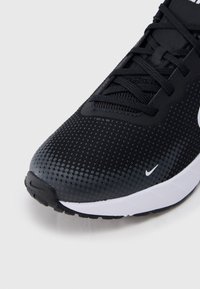 Μαύρο αθλητικό παπούτσι με υφασμένο πάνω μέρος, μαύρα κορδόνια, λευκή μεσαία σόλα και μικρό λευκό λογότυπο Nike κοντά στη σόλα.