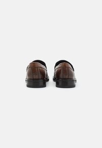 Pantofi din piele maro cu un finisaj neted, formă rotunjită, toc mic negru și cusături decorative subtile pe spate.