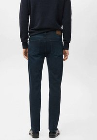 Vaqueros azul oscuro con corte slim, diseño de cinco bolsillos y parche de cuero en la parte trasera. La tela parece suave con un ligero elastano.