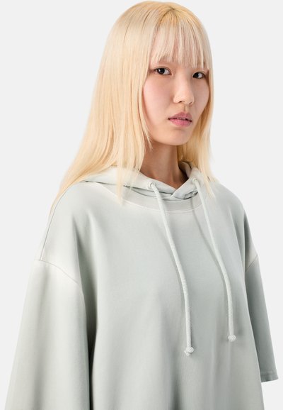 Jasnozielona, oversize bluza z kapturem i sznurkiem, wykonana z miękkiego materiału, z szerokimi rękawami i luźnym krojem zapewniającym komfort.