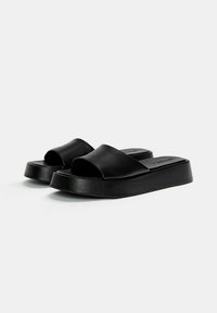 Black platform slide sandals with a wide upper strap, smooth leather texture, and a chunky sole for added height and support.