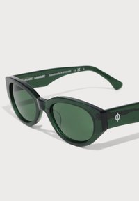 Green sunglasses with a chunky, angular frame, made of glossy material. Dark lenses and subtle logo detailing on the temple. Handmade in Vietnam.
