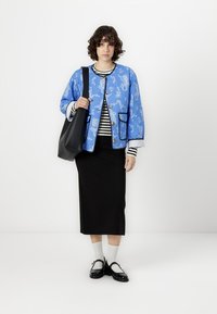 Blue patterned jacket with black trim, black skirt, striped top, white socks, and black shoes. Black handbag is held in one hand.