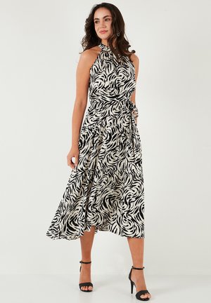 Black and white patterned halter neck dress with a flowing skirt, tied waist detail, and a smooth texture. Strappy black heels complete the look.