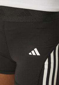 Pantaloni sportivi neri con una ampia cintura nera e un logo discreto. Accenti bianchi a tre strisce sui lati arricchiscono il design.