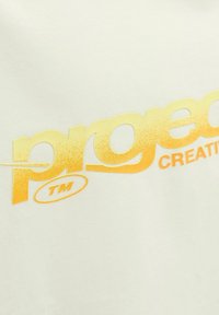 Light beige T-shirt featuring bold yellow text, "project," with a gradient effect and "CREATING" in smaller text, made from soft cotton material.