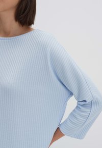 Hellblauses Strickoberteil mit einem strukturierten Muster, weit ausgeschnittenem Bootsausschnitt, Dreiviertelärmeln und lässiger Passform. Glattes Material mit Rippdetail.