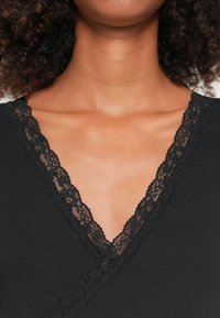 Indumento nero con scollatura a V ornato da un intricato bordo di pizzo nero. La texture è morbida con un motivo a coste.