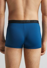 Bañadores azules con una cinturilla elástica negra que presenta el nombre de la marca. Textura suave y diseño ajustado, que llega hasta la mitad del muslo.