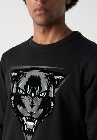 Sudadera negra con un gráfico de la cabeza de un feroz pantera negra con ojos verdes, textura detallada y un acento triangular detrás.