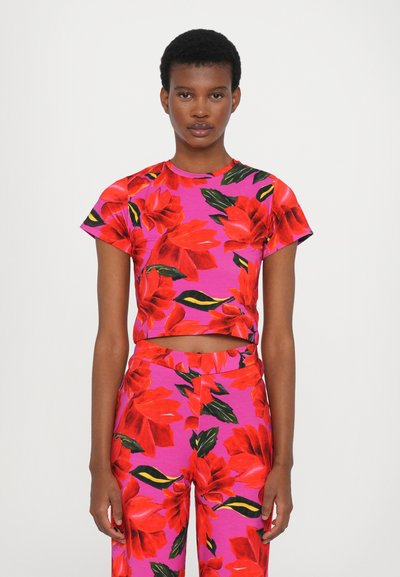 Top corto ajustado y pantalones a juego, ambos en rosa con grandes patrones florales rojos, con mangas cortas y un diseño de abdomen al aire.
