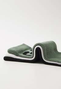 Chaussettes rayées vertes, blanches et noires avec une texture côtelée, ornées d'une inscription noire sur la section verte, reposant en position pliée.