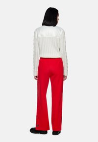 White ribbed knit sweater with a satin back paired with red wide-leg pants. Black chunky shoes complete the outfit.