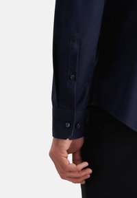 Marineblaue Hemd mit geknöpften Manschetten, das eine glatte Textur und ein kleines gesticktes Design in der Nähe der Manschette aufweist. Reguläre Passform, abgewinkelter Saum.