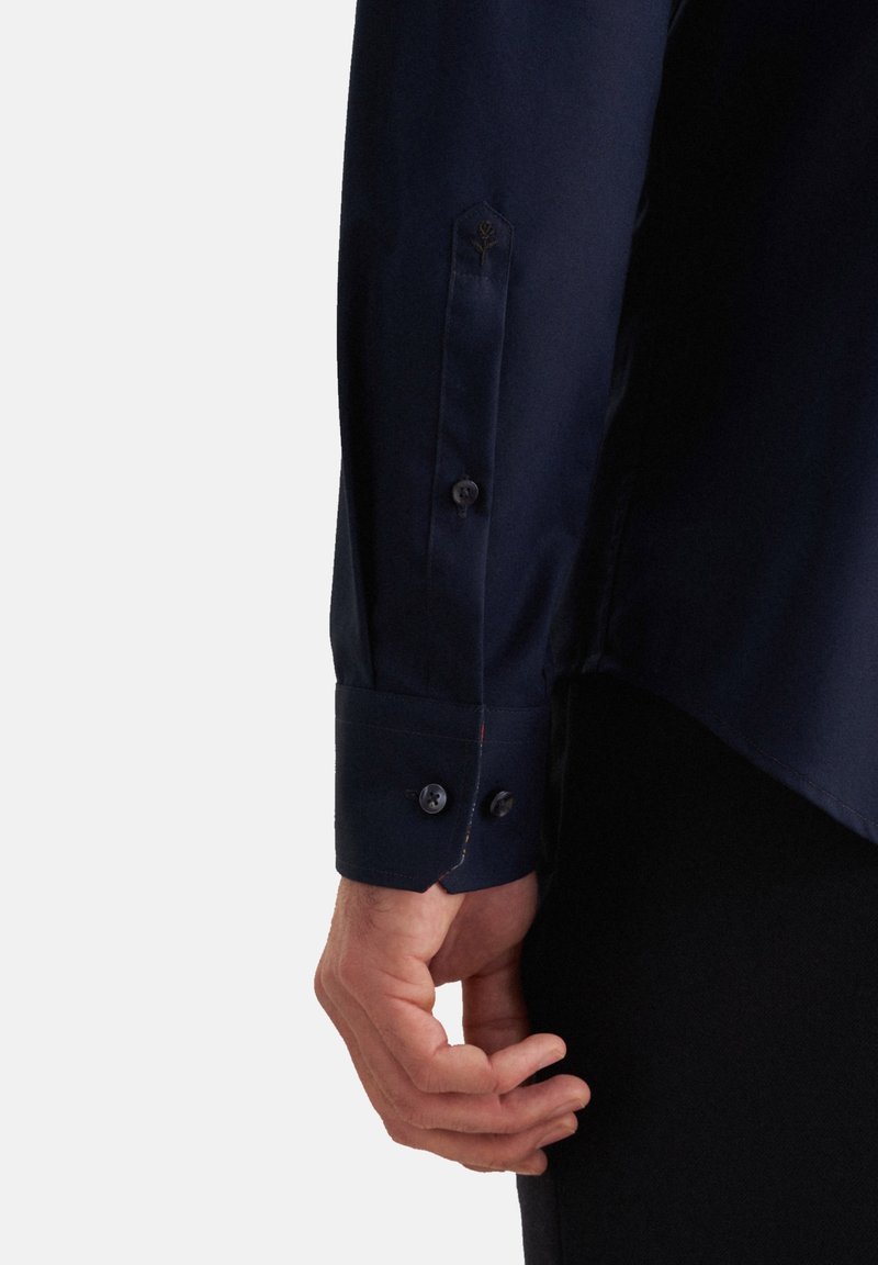 Marineblaue Hemd mit geknöpften Manschetten, das eine glatte Textur und ein kleines gesticktes Design in der Nähe der Manschette aufweist. Reguläre Passform, abgewinkelter Saum.