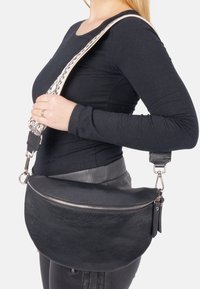 Schwarze Leder-Umhängetasche mit strukturiertem Oberflächen, geschwungener Form, silbernem Reißverschluss und einem gemusterten Träger mit schwarzem Akzent.
