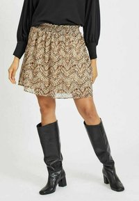 Brun och beige mönstrad mini kjol med smockad midja, tillsammans med knähöga svarta läderstövlar med blockklackar.