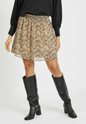 Jupe mini à motifs marron et beige avec taille smockée, assortie à des bottes en cuir noir montantes avec des talons carrés.
