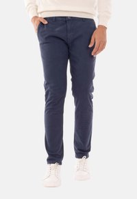 Chino blu navy realizzati in cotone morbido, con un design slim fit, tasche anteriori e chiusura con bottone in vita. Indossati con sneakers bianche.