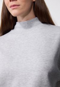Sudadera gris de cuello alto con una textura suave y detalles de costura mínimos. La tela parece suave y ligeramente elástica.