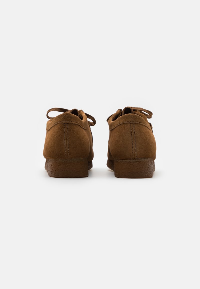 Brown suede shoes with a low heel, rounded toe, and lace-up design. The surface has a soft texture and features stitched accents.