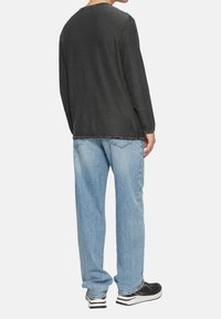 Casual grijs shirt met lange mouwen gecombineerd met lichtblauwe losse jeans. Zwarte sneakers met witte accenten maken de outfit compleet.