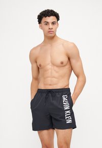 Shorts de bain noirs avec une taille élastique, cordon de serrage et logo "Calvin Klein" blanc sur le côté. Tissu lisse et léger.
